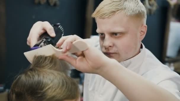 Cabeleireiro loiro profissional fazendo um novo corte de cabelo no cabelo molhado com a ajuda de pente e barbeador elétrico. Barbeiro masculino. Novo corte de cabelo — Vídeo de Stock