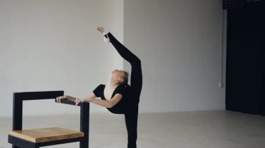 Sevimli kız beyaz spor okulda jimnastik uygulamaları, o tek ayak üstünde duran bölmelerini esniyor iken ve elini sandalyenin üzerine yaslanmış. Bale Okulu, profesyonel dans