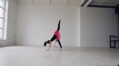 Şirin Jimnastikçi daire pencere arka plan üzerinde beyaz Studio bacaklarda topuz ile yapıyor. Jimnastik kız siyah elbise ve pembe etek giymiş