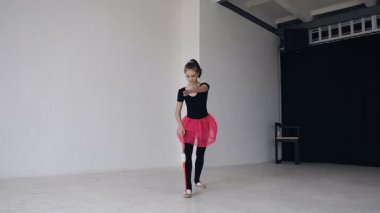 Şirin Jimnastikçi topuz beyaz zemin üzerine stüdyoda bacaklarda daireyle yapıyor. Jimnastik kız siyah elbise ve pembe etek giymiş. Jimnastik salonu