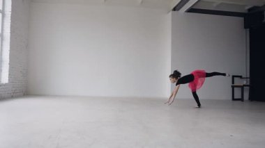 Jimnastik okul. Şirin Jimnastikçi kız bir backflip elleriyle geniş beyaz balo salonunda gerçekleştirir. Esnek kız iki akrobatik flip yapıyor. Siyah elbise ve pembe etek giymiş kız