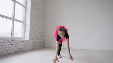 Jimnastik okul. Şirin Jimnastikçi kız bir backflip elleriyle geniş beyaz balo salonunda gerçekleştirir. Esnek kız üç akrobatik flips yapıyor. Siyah elbise ve pembe etek giymiş kız