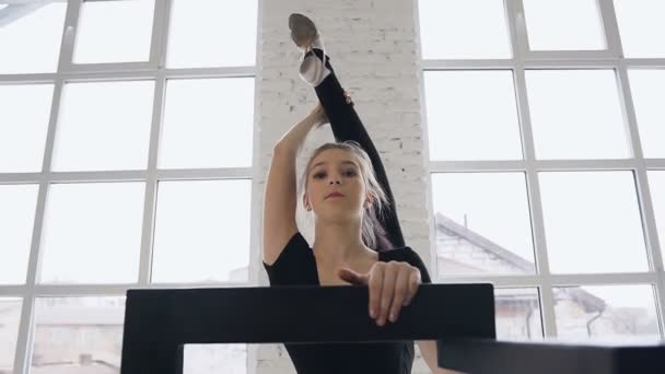 Flexibla söt tjej gymnast värmer upp hon tittar i kameran. Vacker flicka i sportkläder gör yogaövningar. Flickan övar gymnastik i en sporthall, hon sträcker, splittringar som står på — Stockvideo