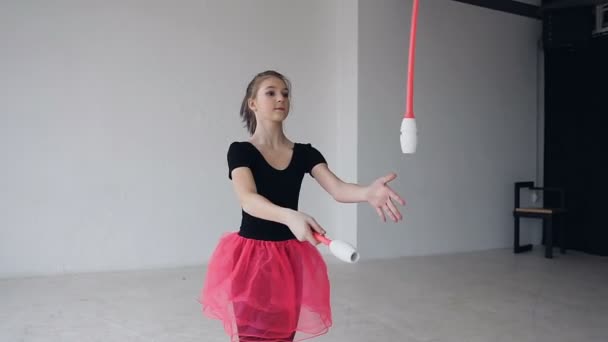 Gymnaste fille tourne les masses. Fille gymnaste habillé corps noir et jupe rose avec des messes dans les mains tournent autour d'elle à l'école de sport, dans le fond blanc — Video