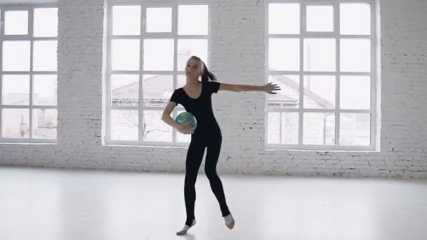 Die niedliche Teenie-Turnerin trainiert mit Ball auf weißem Hintergrund vor großen Fenstern in der Turnschule. Sport, Stretching, Beweglichkeit, Aerobic — Stockvideo