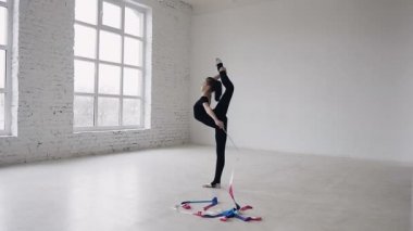 Küçük jimnastik jimnastik yaparken siyah gövde renkli bir şerit beyaz Studio ile egzersiz. Sevimli kız germe egzersiz spor salonunda yapar..