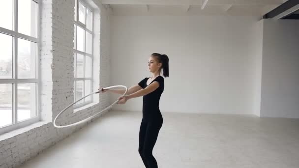 Joven chica atractiva en cuerpo negro realiza el entrenamiento de un ejercicio de gimnasia con un aro en la escuela de gimnasia sobre fondo blanco — Vídeo de stock