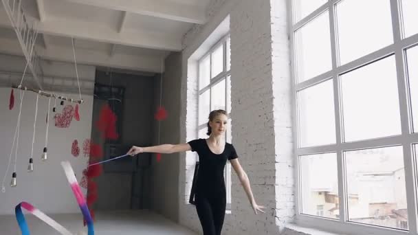 Atrakcyjna dziewczyna nastolatek gimnastyczka taniec z kolorowe wstążki w siłownia sport w tle w pobliżu okna. Atrakcyjny dziewczynka gimnastyczka skoki z wstążki w sport Szkoła — Wideo stockowe