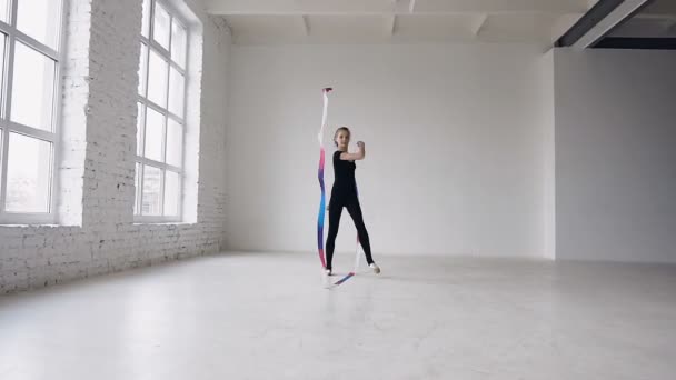 Sarışın genç kız dans ritmik jimnastik, spor okulunda beyaz arka planda siyah gövde renkli kurdele ile modern — Stok video