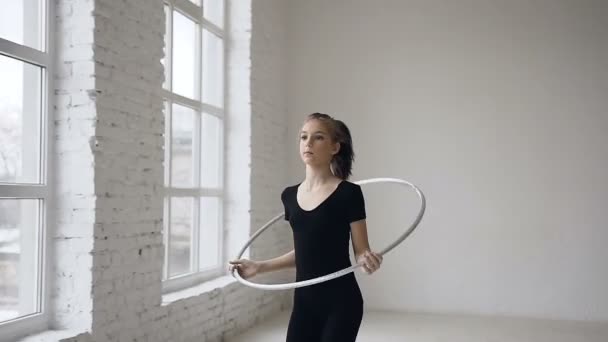 Gimnasia rítmica: chica gimnástica vestida de negro body realiza entrenamiento un ejercicio de gimnasia con un aro en la escuela de deporte — Vídeo de stock