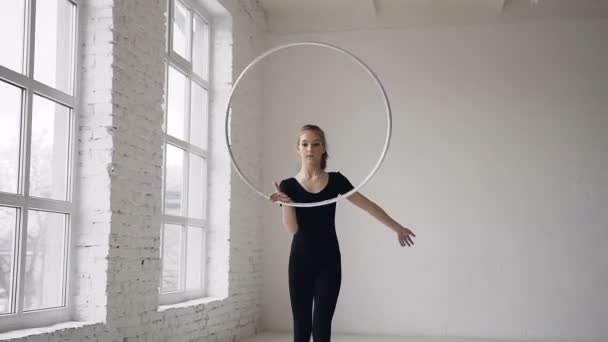 Porträtt av söt attraktiva glad flicka i svart kropp spinning bågen å i gymnastiska skolan på vit bakgrund och tittar på kameran — Stockvideo