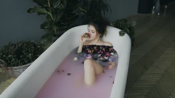 Hermosa mujer joven que se relaja en el baño de leche con muchas flores fragantes hermosas. Tratamientos de spa y cuidado de la piel — Vídeo de stock