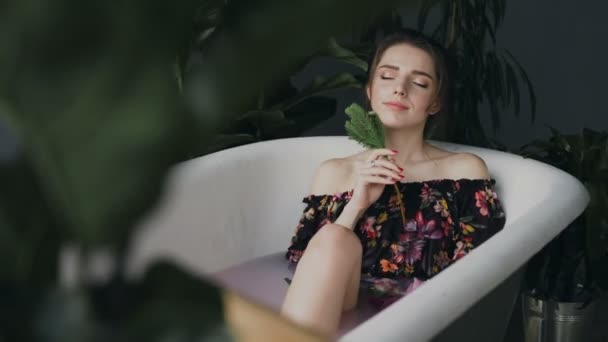 Jovem mulher sexy relaxando em um banho quente no centro de spa. Menina bonita no banho com flores perfumadas relaxando com os olhos fechados. Cuidados corporais e tratamentos de spa — Vídeo de Stock