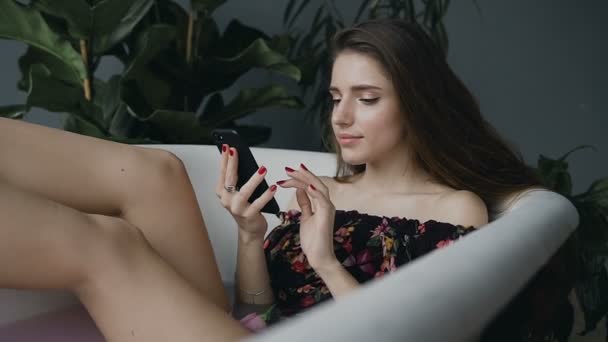das Mädchen entspannt sich in der warmen Milchwanne und benutzt ihr Handy. ein schönes junges Mädchen benutzt ein Telefon, während sie in einem warmen Milchbad sitzt und entspannt
