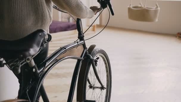 Fecho recortado, visão traseira de uma menina descansando no guidão de sua bicicleta de engrenagem fixa vintage em ambientes fechados — Vídeo de Stock