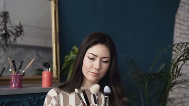 Maskérka mladá žena drží štětce na make-up v salonu krásy. Sada kosmetických štětců v Dámské ruce ve studiu krásy. Příslušenství pro vzhled — Stock video