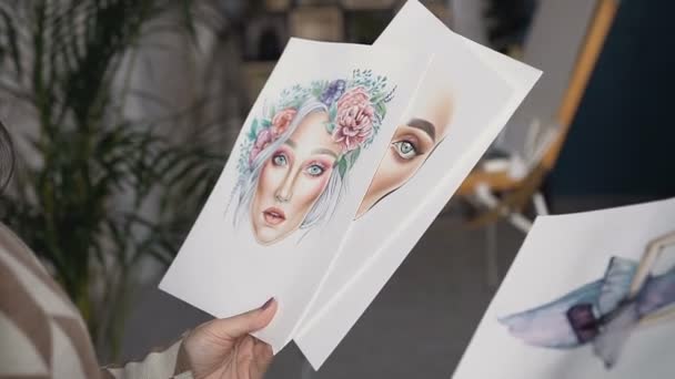 A young woman looks at sketches of design work at beauty salon. Good work of the artist. Beautiful young fashion designer woman working at art studio. Face chart — Stock Video