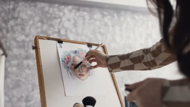 Die Künstlerin für Make-up und Schönheit kreiert mit Aquarellpapier, Schatten, Lippenstiften und Rouge im Atelier ein schönes Gesichtsschminkdiagramm. junge Frau im hellen Studio zeichnet ein Gesichtsdiagramm — Stockvideo
