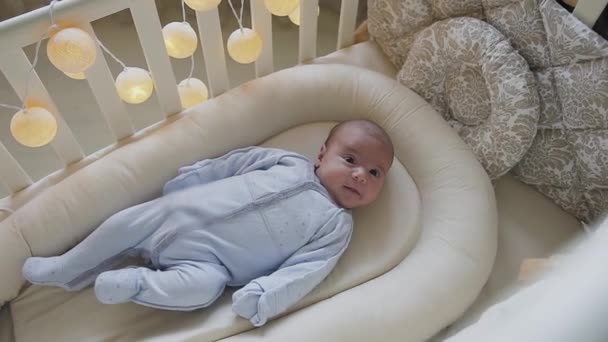 Newborn baby boy lying in the crib looks at camera and smiling. Cute little baby lying in the crib at home. Baby boy — Stock Video