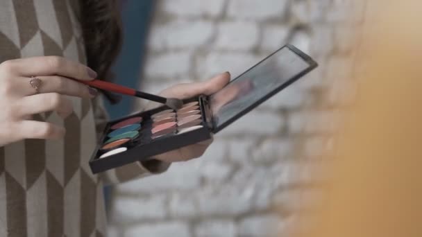 Close-up. A professional make-up artist picks up shadows on the brush. Make-up young woman artists hand with brush and eye-shadow palette — Stock Video