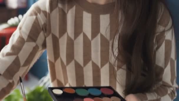 Wizażystka młoda kobieta używa odcień paleta do malowania twarzy wykresu. Artysta maluje wykres twarz na płótnie i rozmazuje małego pędzla przy użyciu palety cieni kosmetyki — Wideo stockowe