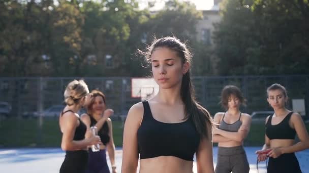 Hermoso retrato de chica bastante atlética de 30 años en ropa deportiva mirando a la cámara después de entrenar al aire libre en el fondo del equipo de fitness femenino — Vídeos de Stock