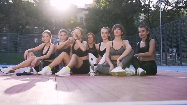 Привлекательная фотография счастливых улыбающихся стройных спортивных девушек с поднятыми руками, которые отмечают окончание совместной тренировки в парке — стоковое видео