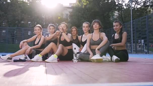 Atractiva imagen de las niñas deportivas delgadas sonrientes felices con las manos levantadas que celebran el final de su entrenamiento de fitness conjunto en el campo de deportes del parque — Vídeos de Stock