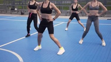 Sportif kısa tişörtlü ve spor şortlu hoş bir bayan eğitmen. Parktaki spor grubuna atlama bacakları egzersizleri gösteriyor.