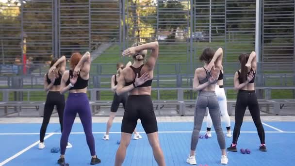 Vista posterior de mujeres jóvenes y deportivas desconocidas que se cierran las manos detrás de la espalda durante el entrenamiento de fitness en el parque — Vídeo de stock