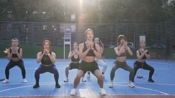 Pohled zepředu na ženský fitness tým, který při západu slunce provádí squat cvičení na venkovním hřišti — Stock video