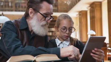 Zeki, sakallı, gözlüklü, yakışıklı torunuyla kütüphanede oturan ve tablet bilgisayarı kullanarak öğrenme yeteneği olan büyük baba.