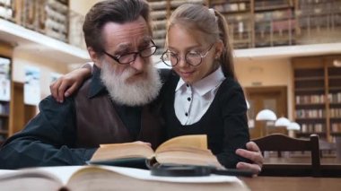 Güzel bir çift torunun çekici portresi ve kütüphanede oturup kitap okuyan yaşlı sakallı büyükbabası.