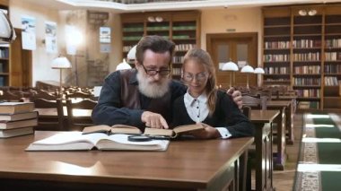 Mutlu, yaşlı, sakallı, mutlu büyükbabası ve güzel, genç torunu kütüphanede birlikte kitap okuyorlar.