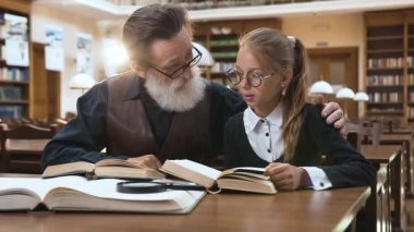 Kütüphanede oturup birlikte kitap okuyan mutlu büyükbaba ve torunun harika portresi.