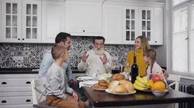 Mutlu gülümseyen aile, çocuklar ve büyükbaba Şükran Günü 'nde şenlik masasında bir araya geliyorlar.