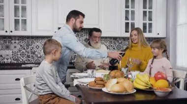 Sevimli mutlu aile Şükran Günü 'nü kutlamak için şenlik masasında toplanırken çekici bir adam kadehlere şarap dolduruyor.