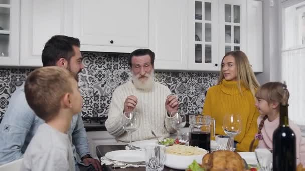 Aantrekkelijke familie van man, vrouw en hun kinderen met gerespecteerd grootvader zittend aan de Thanksgiving tafel en pratend — Stockvideo