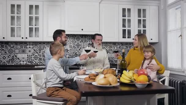 Glücklich lächelnde Familie feiert Erntedank mit erhobenen Gläsern am festlichen Küchentisch sitzend — Stockvideo