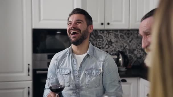 Guapo joven con barba bien arreglada riendo sinceramente, sentado hormiga la mesa de Acción de Gracias con su familia — Vídeo de stock