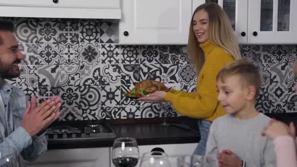 Hoog-pittige mooie vrouw in gebreide trui brengen gebraden kalkoen naar de feestelijke tafel waar zitten haar hele familie met gerespecteerde oude man — Stockvideo