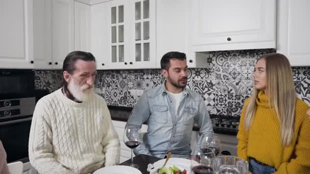 Приємна весела сім'я зі старим бородатим дідусем сидить навколо святкового столу і молиться перед сімейною вечерею на кухні — стокове відео