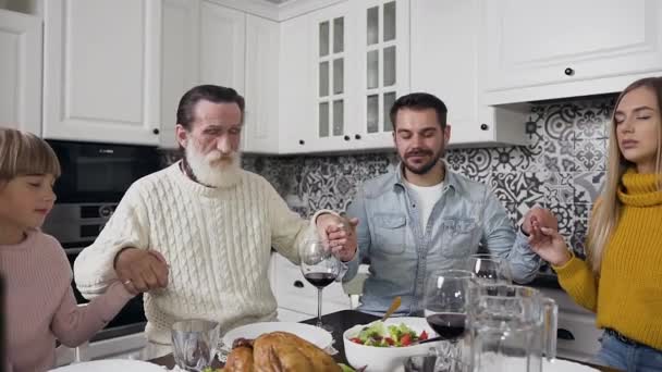 Atrakcyjna rodzina ze starym męskim pokoleniem trzymającym się za ręce i modlącym zamkniętymi oczami przy świątecznym stole — Wideo stockowe
