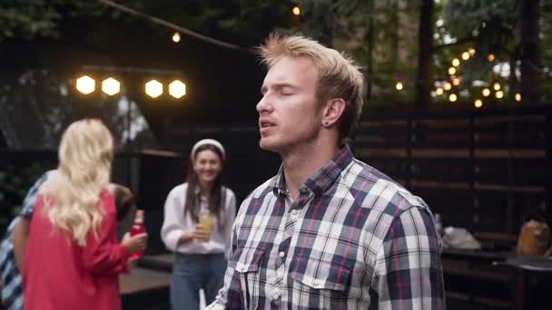 Handsome young guy in plaid shirt enjoying his dancing under inflammatory music on the background of his people company at diverse party in cozy evening — Stock Video