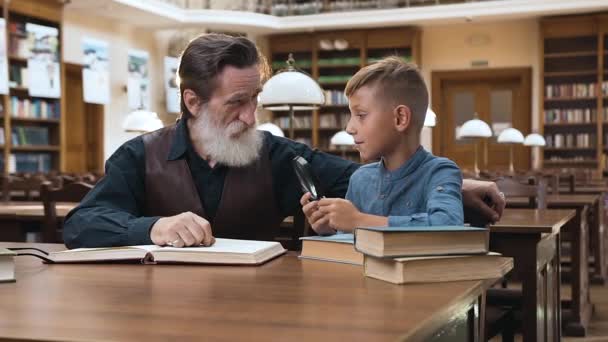 Yakışıklı bilge sakallı büyükbaba ergen torunuyla kütüphanede vakit geçiriyor. — Stok video