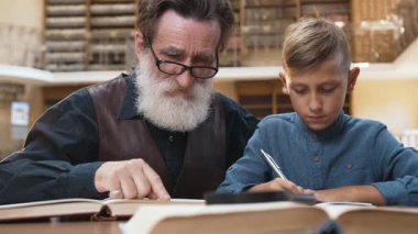 Kütüphanede birlikte kitap okuyan zeki sakallı büyükbaba ve yakışıklı okul çocuğu.