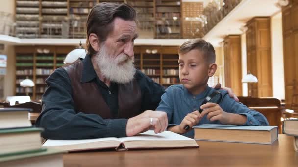 十代の孫に本を読むことの重要性を説明する快適なひげそりの男の正面図 — ストック動画