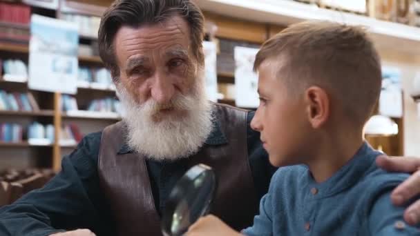 Attractive teen schoolboy carefully listening his senior respected grandfather telling about books — Stock Video