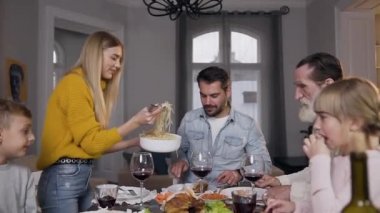 Gülümseyen büyüleyici kadın aile yemeği sırasında tüm akrabaları için tabağa spagetti koyar.