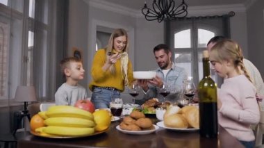 Gülümseyen sarışın anne aile ziyafetinde tabağa spagetti koyuyor.